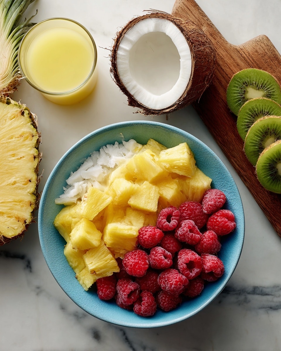 A bright blue bowl filled with two layers of fruit: one half with yellow pineapple chunks and the other half with red raspberries, both textures clear and fresh. Around the bowl, there are two open coconut halves showing white coconut flesh inside, a whole pineapple top edge visible, a glass filled with yellow juice on the left, and sliced green kiwi fruits on a wooden board to the right. All items sit on a white marbled surface. photo taken with an iphone --ar 4:5 --v 7