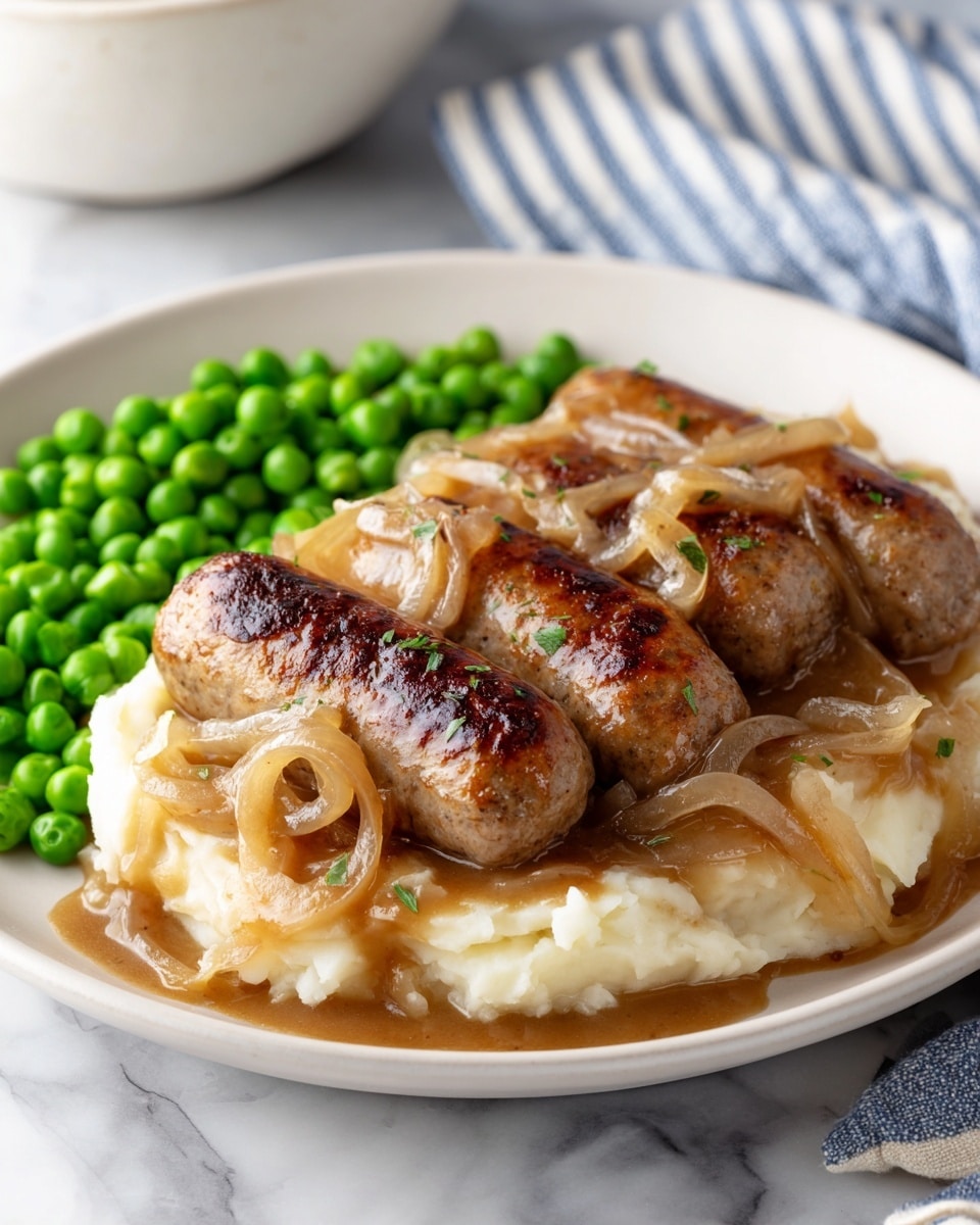 On a white plate, there is a thick layer of creamy mashed potatoes spread evenly across the bottom. On top of the mashed potatoes, there are three browned sausages placed close together, partially covered by a glossy brown onion gravy with visible soft onion slices. To the side of the sausages and mashed potatoes, there is a neat pile of bright green peas, adding a pop of color to the plate. The plate sits on a white marbled surface with a blue striped cloth partially visible in the background. Photo taken with an iphone --ar 4:5 --v 7