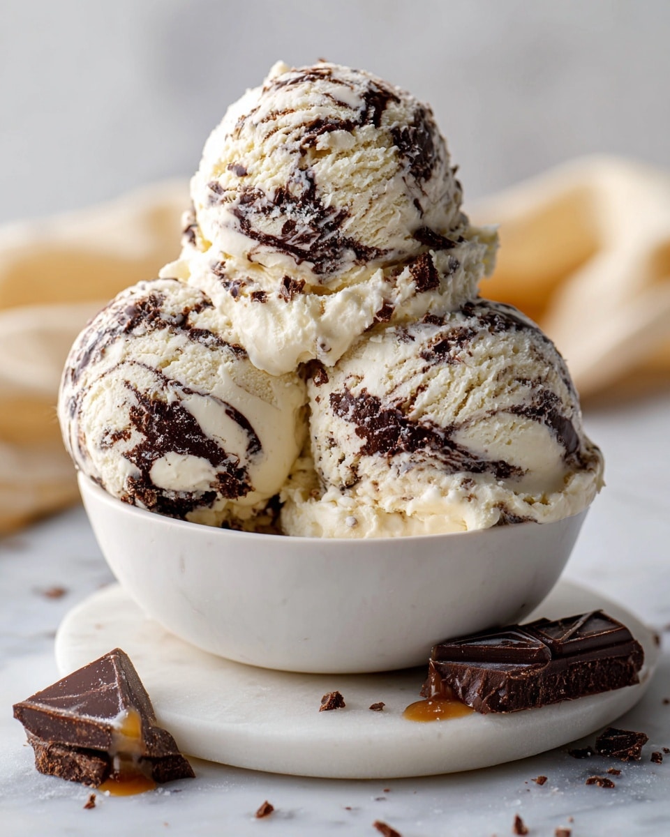 The image shows three scoops of ice cream with white and brown swirls, placed inside a white bowl. The ice cream has a creamy texture with visible chocolate or caramel ribbons mixed inside each scoop. The bowl is set on a white marbled surface, with a small piece of a two-colored candy or chocolate near the front. The background is softly lit and clean, emphasizing the ice cream's smooth and swirled layers. Photo taken with an iphone --ar 4:5 --v 7
