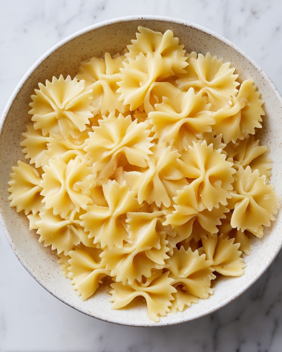 A close-up view of a white speckled bowl filled with plain cooked farfalle pasta, also known as bow-tie pasta. The pasta is light yellow, smooth, and slightly shiny, with each piece showing the distinct butterfly shape with pinched centers and flared edges. The pasta fills the bowl evenly, showing various pieces overlapping each other with soft shadows and highlights that make the texture and shape clear. The bowl sits on a white marbled surface. photo taken with an iphone --ar 4:5 --v 7