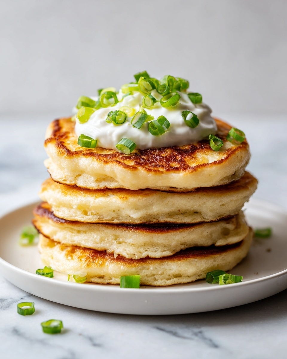 A stack of four thick, golden pancakes with light brown edges sits on a white plate on a white marbled surface. On top of the stack is a smooth layer of white cream, decorated with plenty of chopped green onions that add a fresh green color. Additional small pieces of green onion are scattered around the base of the plate. The pancakes have a soft and fluffy texture, with slight browning on the top. Photo taken with an iphone --ar 4:5 --v 7
