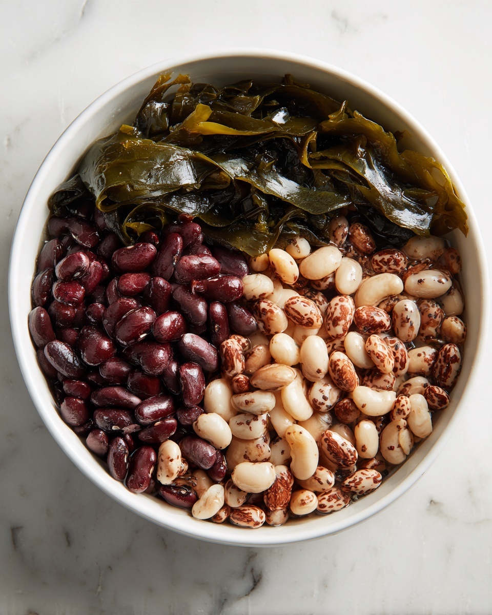 New England Baked Beans Recipe 4 A white bowl filled with a mix of three types of beans: dark red, light brown with speckles, and white with dark brown speckles, covering the entire bottom and spreading towards the edges. On top, two dark green, glossy sheets of seaweed lay flat, partially overlapping near the upper left side of the bowl. The bowl rests on a white marbled surface. photo taken with an iphone --ar 4:5 --v 7