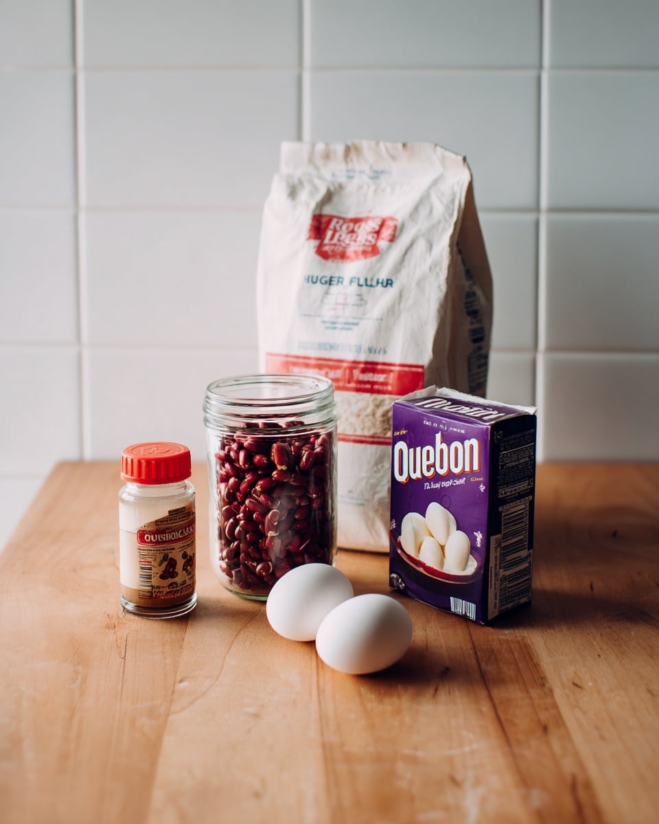 The image shows a wooden table with a white tiled wall behind it. On the table are five items arranged in a small cluster: a white bag of Rogers all-purpose flour standing at the back, a clear glass jar filled with red beans or seeds with a red and white label to the left front, a small bottle of vanilla extract with a red lid in front center, a purple carton of cream with