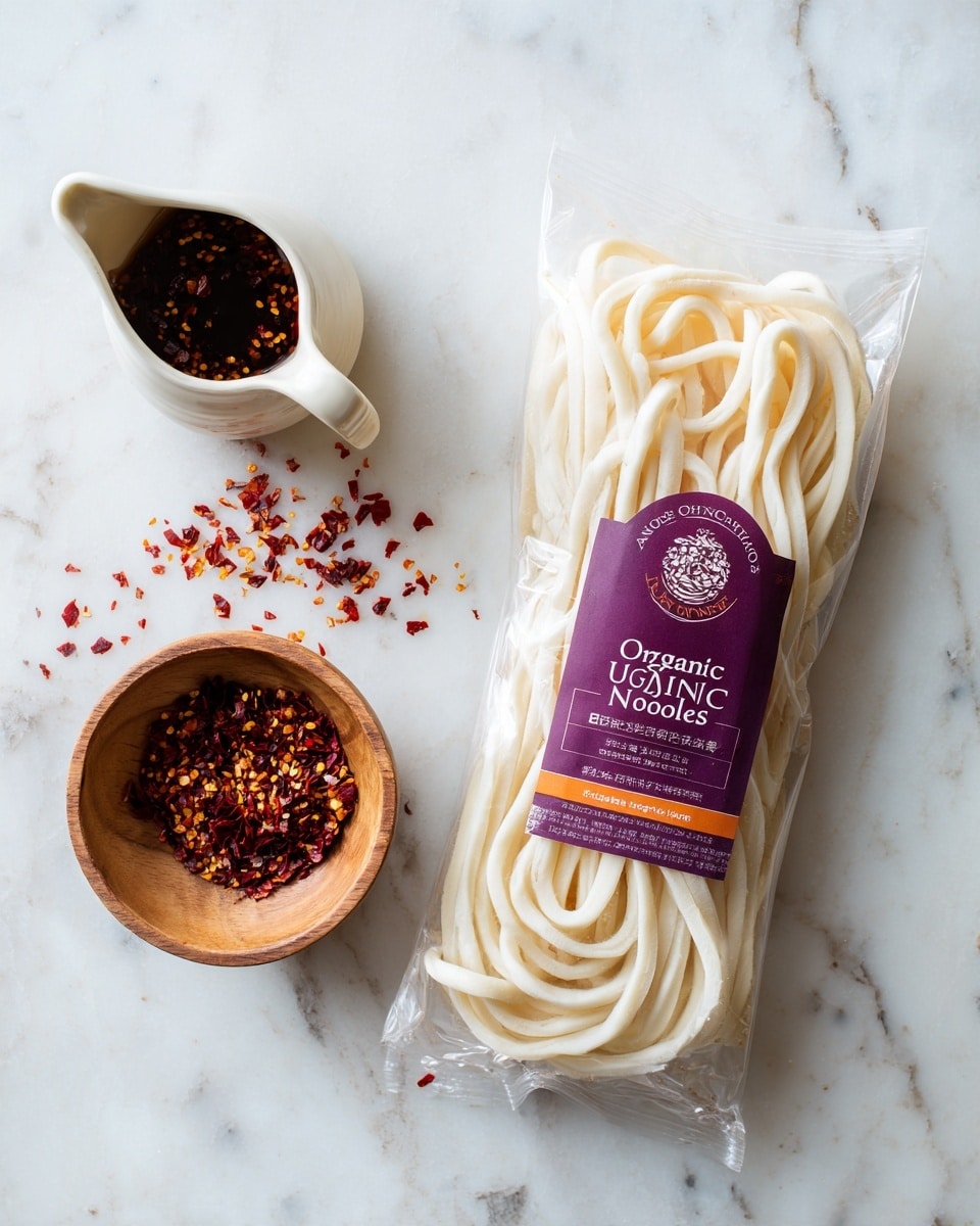 A clear plastic package of Annie Chun's Organic Udon Noodles is placed on a white marbled textured surface. The top of the package is purple with the brand's logo, and the middle is white with