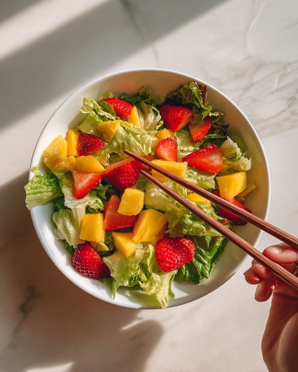 A white bowl filled with a fresh salad showing three visible layers: the bottom layer has light green leafy lettuce with a soft, slightly wilted texture; the middle layer contains bright yellow pineapple chunks with a juicy, fibrous texture; the top layer has vibrant red strawberry slices scattered evenly, their smooth and shiny surfaces contrasting with the other ingredients. The salad is on a white marbled surface, with a pair of light wooden chopsticks placed to the right side. photo taken with an iphone --ar 4:5 --v 7