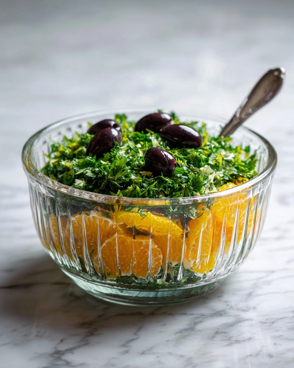 The image shows a clear glass bowl filled with a colorful salad. The bottom layer has bright orange segments with a shiny, slightly wet texture. Over the orange pieces, there is a fresh layer of chopped green parsley leaves, adding a rough and leafy texture. On top of the parsley, small black olives are scattered evenly, creating a smooth and glossy look. The bowl sits on a white marbled surface. photo taken with an iphone --ar 4:5 --v 7