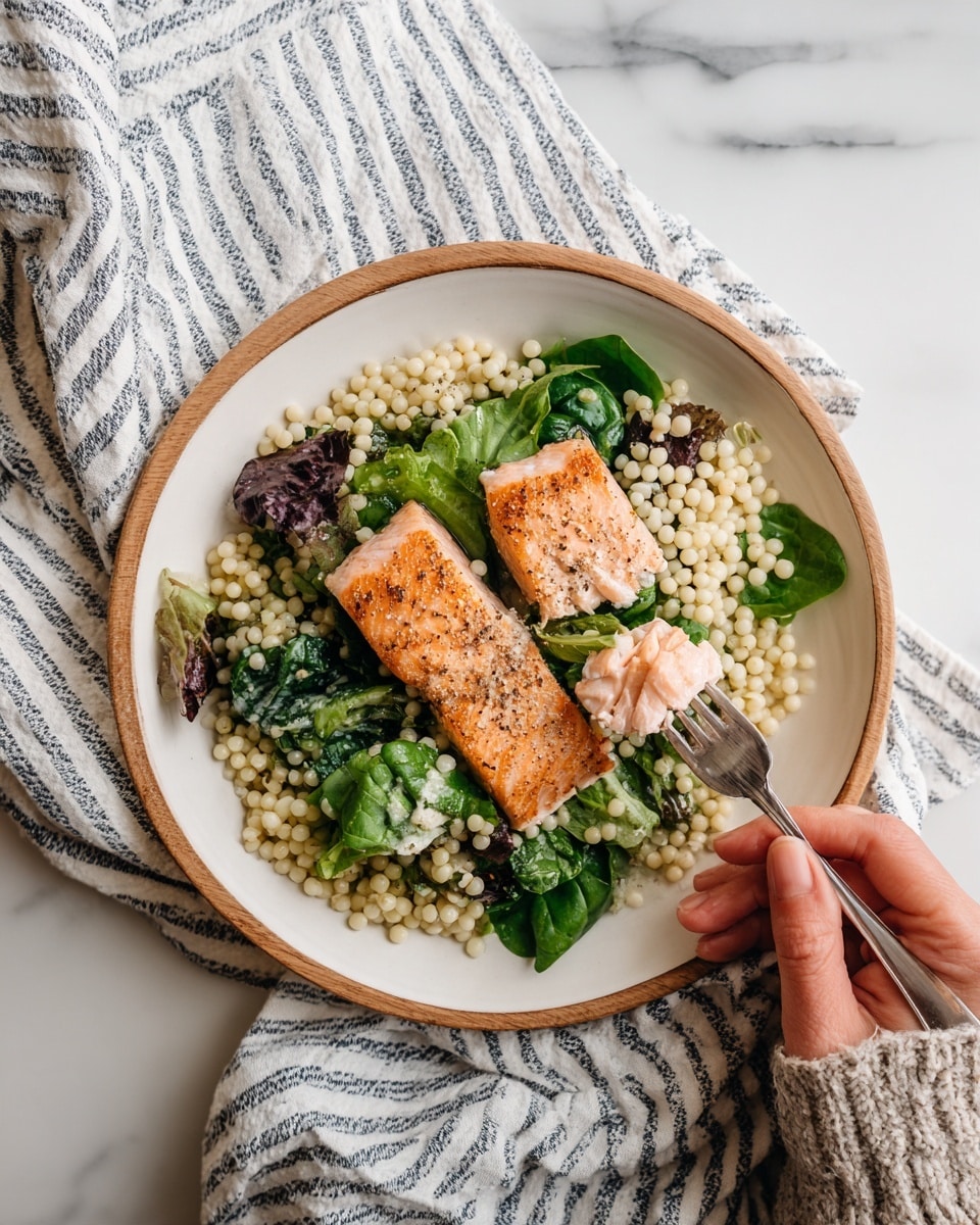 The image shows a wooden round plate holding a meal with three main layers: the bottom layer is a bed of small, round, pale beige couscous pearls spread across the plate; on top of the couscous, there are several pieces of mixed salad leaves, including green and purple shades, with a smooth texture; the top layer consists of two pieces of browned salmon fillets, one partially flaked with a fork, displaying a light pink inside and a crispy brown outside, garnished with thin green herbs. A silver fork rests on the plate, and the plate sits on a white and navy striped cloth on a wooden board with a white marbled surface beneath. Photo taken with an iphone --ar 4:5 --v 7