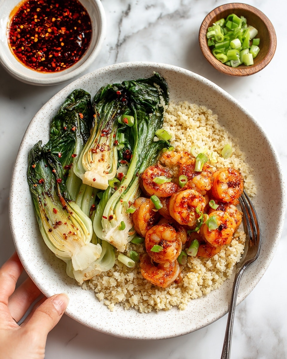 A white speckled bowl holds a meal with three layers: the bottom layer is light beige cauliflower rice with a soft, grainy texture covering the whole base, the middle layer has five grilled shrimp coated in a red chili flake sauce arranged over the rice near the center, and the top layer contains three charred baby bok choy halves with dark green, slightly wilted leaves and white stems positioned on one side of the bowl. Thinly sliced green onions are scattered on the shrimp and bok choy. A fork with a white handle rests on the left edge of the bowl. The bowl sits on a white marbled surface, with small wooden and white bowls of green onions and chili sauce nearby. photo taken with an iphone --ar 4:5 --v 7