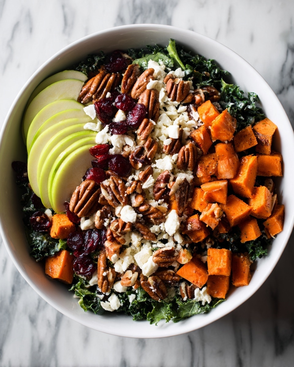 In a white bowl, there is a colorful salad with multiple layers. The bottom layer is made of dark green kale leaves, slightly curly and fresh. On top, there are bright orange sweet potato pieces, soft and cut into thick cubes, scattered all over. Light green apple slices with smooth skin are placed evenly around the bowl. Small white crumbles of cheese sit on top, giving a soft texture. Dark brown pecan nuts are placed throughout, adding a shiny and smooth surface. Bright red dried cranberries are spread evenly, adding a chewy contrast. Everything rests on a white marbled surface, creating a clean and fresh look. photo taken with an iphone --ar 4:5 --v 7